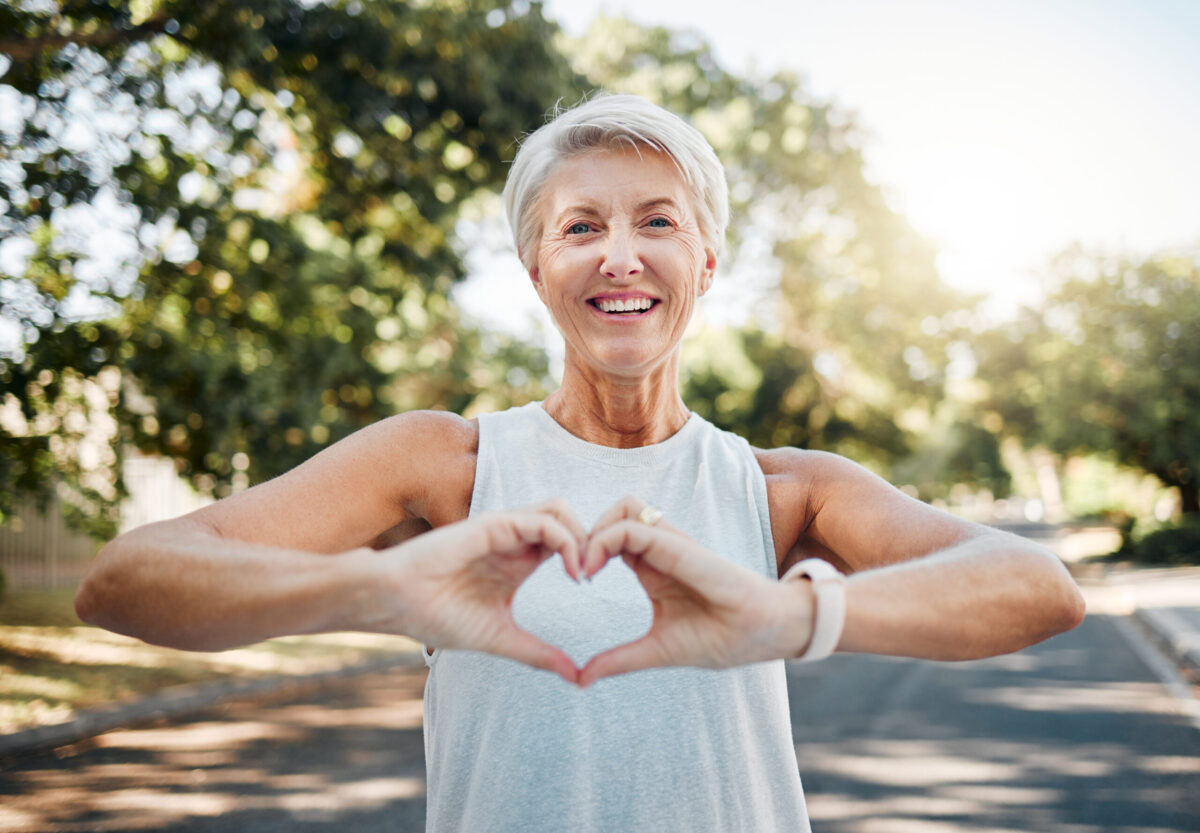 Fitness, happy and heart hands of old woman in nature after running for health, wellness and workout. Smile, motivation and peace with senior lady and sign for love, faith and training in nature.